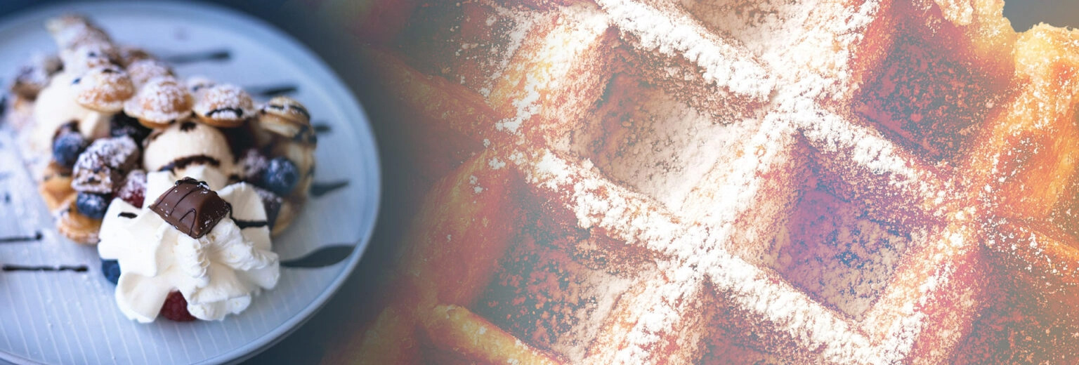 Nahaufnahme von frischer Waffel mit Puderzucker und Sahne sowie Beeren und Schokolade